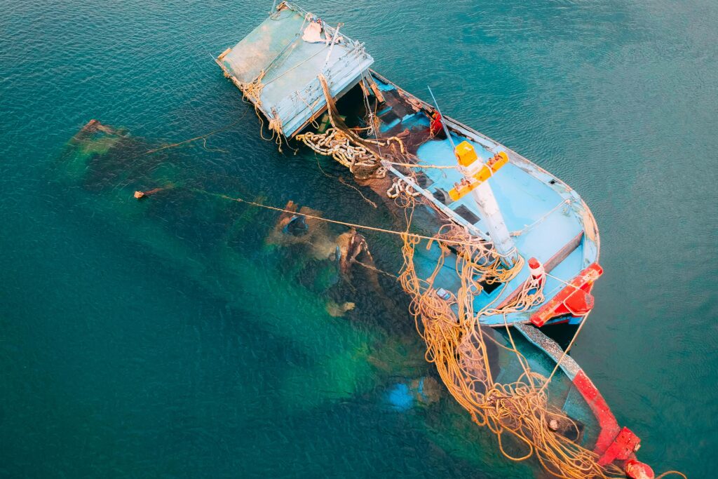 Sunken fishing boat entangled in ropes, partially submerged in the ocean.